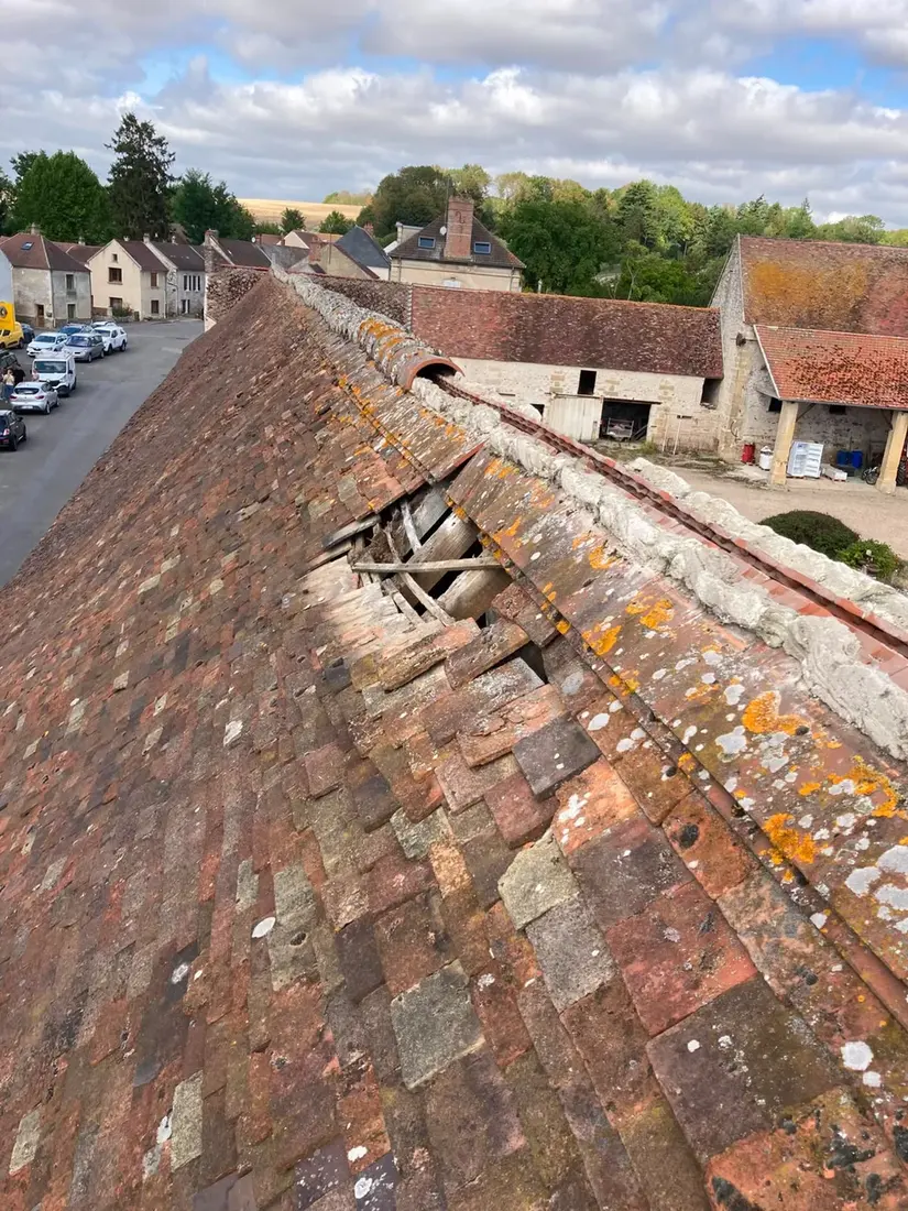 Toiture en tuiles plates anciennes avec un trou dans la couverture près du faîtage