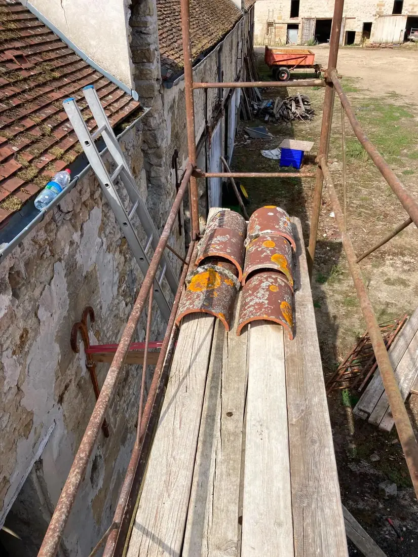 Tuiles faîtières anciennes déposées et triées sur les planches d'un échafaudage