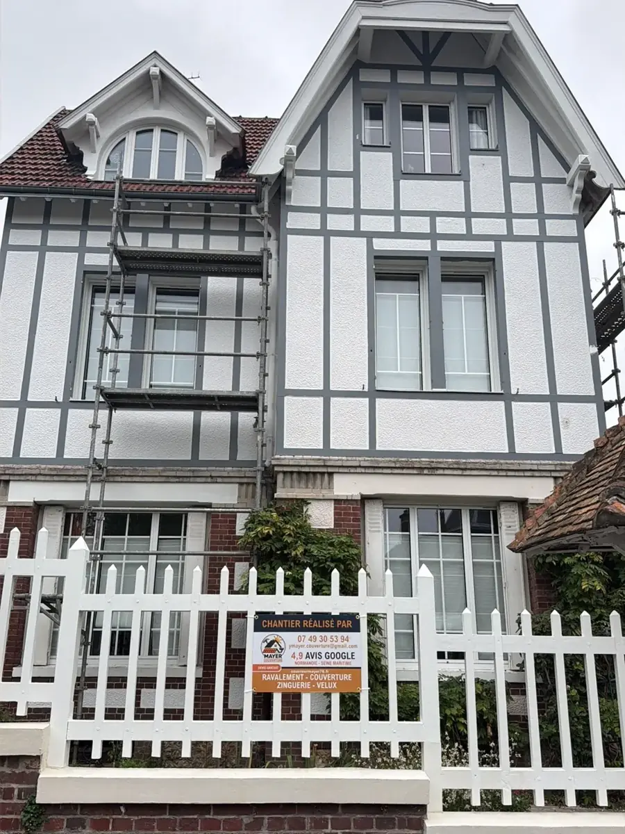 Maison normande à colombages gris et enduit blanc après ravalement, échafaudage encore en place et panneau de chantier Mayer Couverture devant la grille