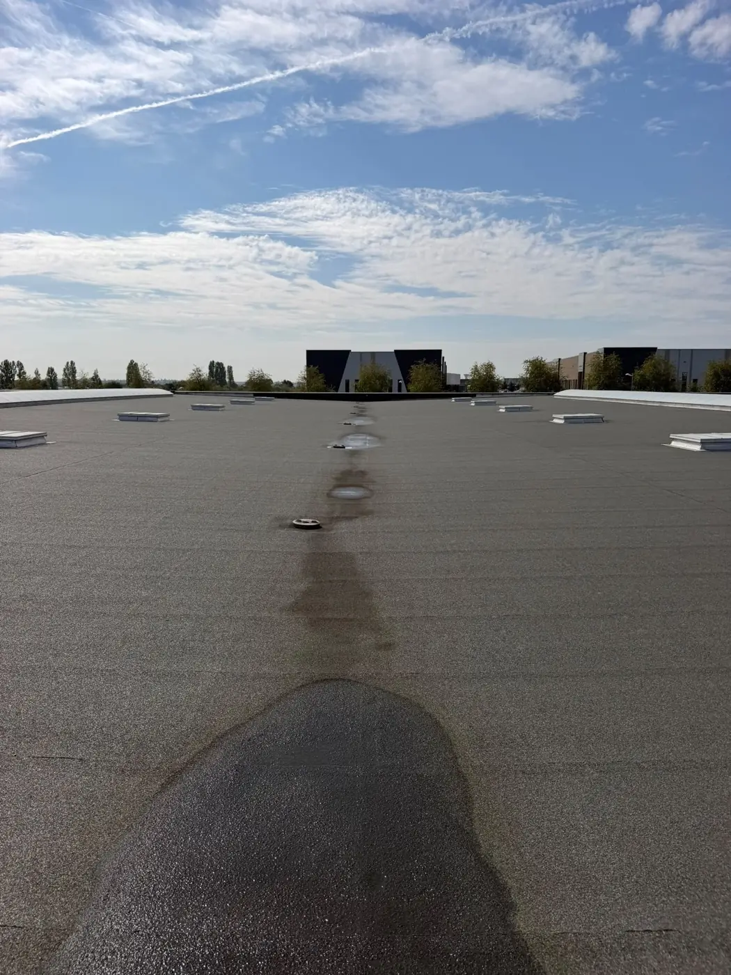 Ligne d'avaloirs d'eaux pluviales alignés le long du fil d'eau d'une toiture-terrasse en bitume autoprotégé