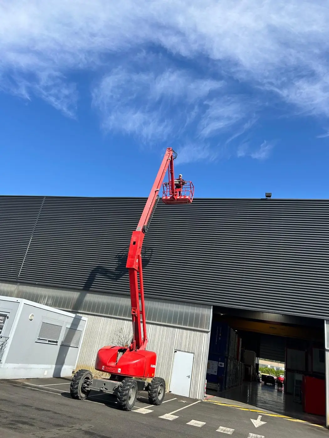 Nacelle télescopique déployée le long d'un bâtiment industriel pour accéder à la toiture-terrasse